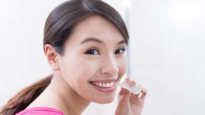 woman smiling as she puts on her Invisalign aligner tray